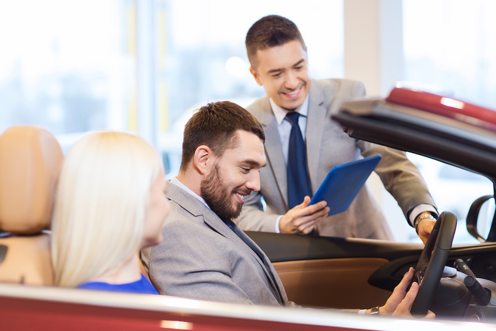 glückliches Paar mit Autohändler in Autoshow oder Salon