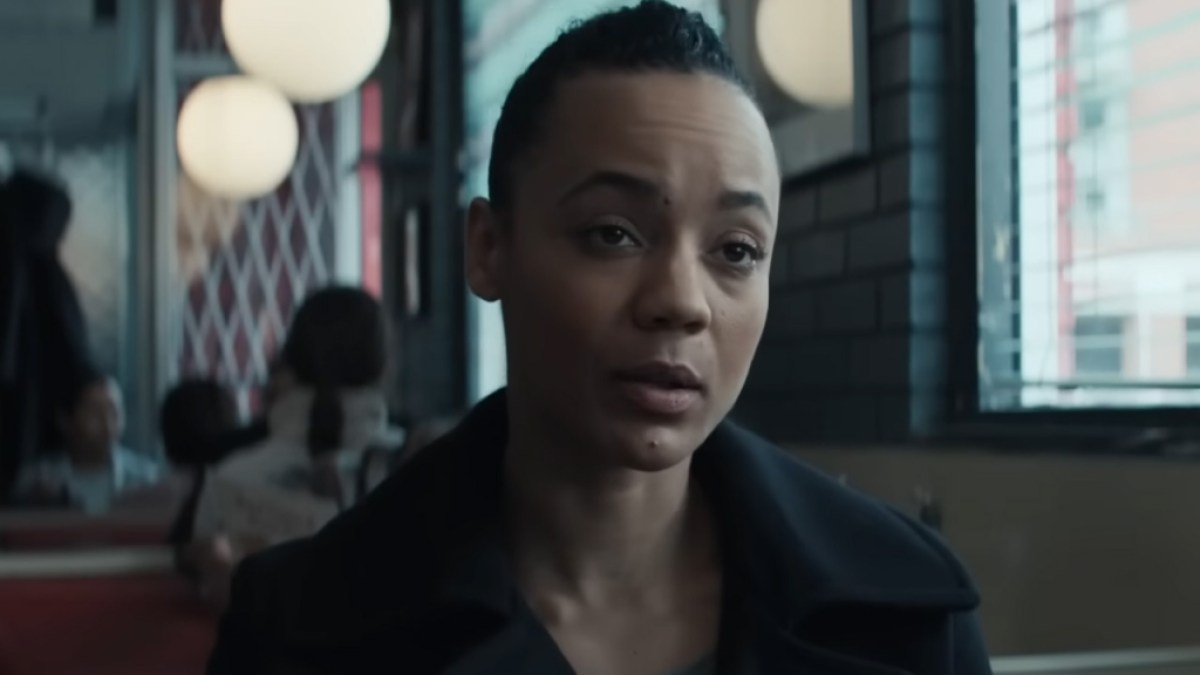 Eine kurzhaarige Frau in einem schwarzen Mantel sitzt in einem Diner in Reacher. 