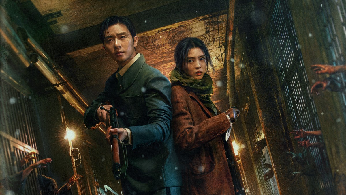 Park Seo-Joon and Han So-Hee hold weapons in a corridor, while hands reach through bars towards them in a still from Gyeongseong Creature.