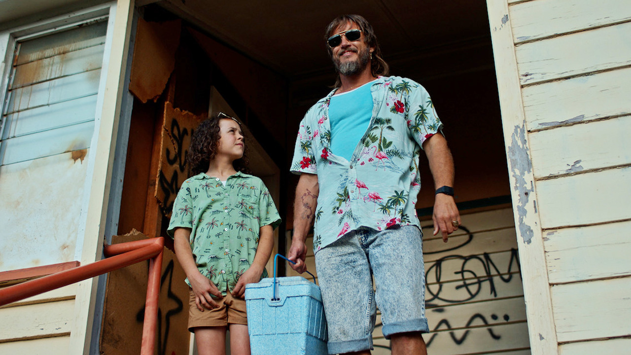 A young boy standing next to a bearded man with a beer cooler.